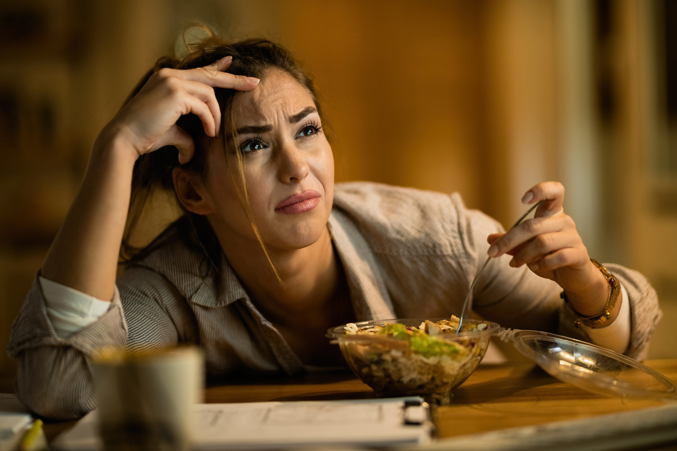 Displeased woman feeling confused while reading an e-mail on a computer and eating salad at night.